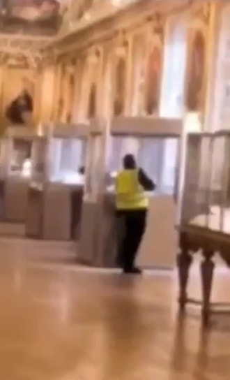 Скриншот из видео, на котором предполагаемый грабитель в желтом жилете, выдав себя за сотрудника музея, при посетителях вскрывает витрину с экспонатами